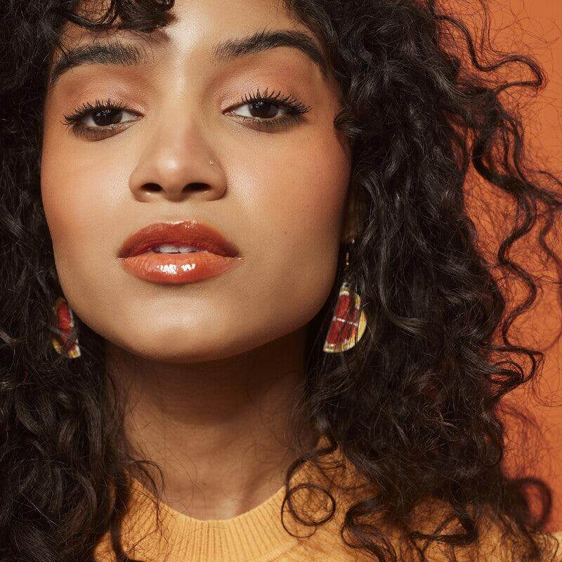 Model showcasing e.l.f Big Mood Mascara with defined lashes and glossy lips against an orange backdrop.