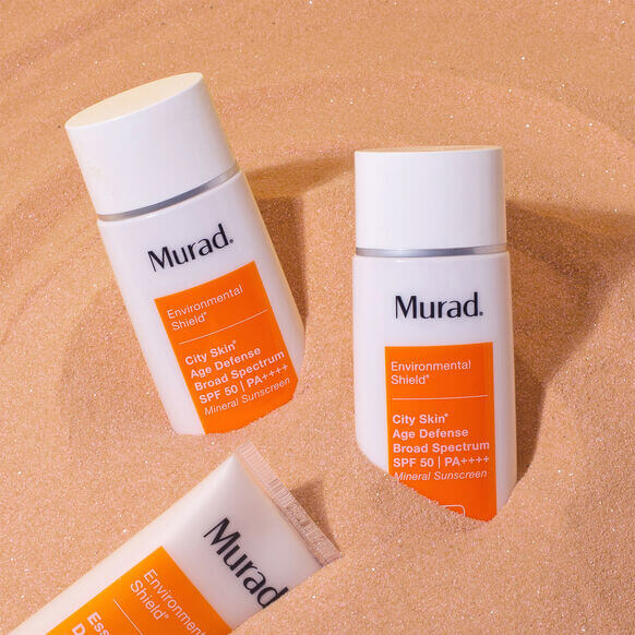 Two bottles of Murad sunscreen on a sand-like textured background