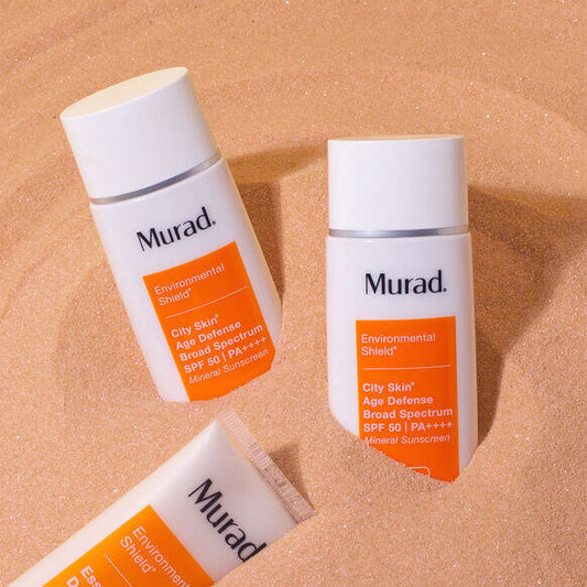 Two bottles of Murad sunscreen on a sand-like textured background