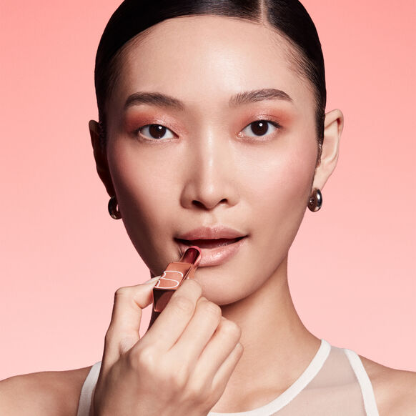 Woman applying NARS lipstick against a pink background