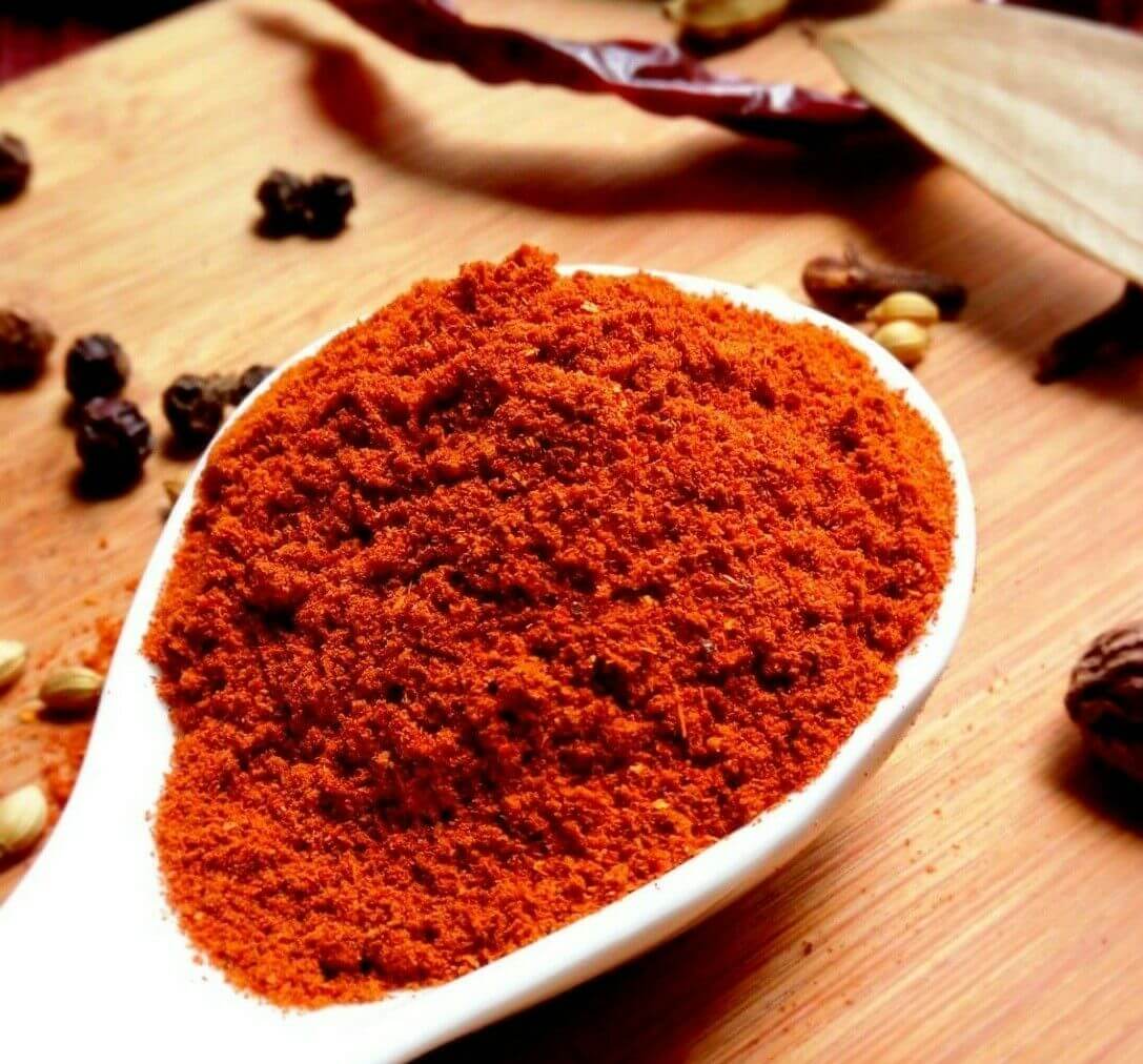 Natco Tandoori Masala in a white spoon, vibrant red spice blend for authentic tandoori cooking.