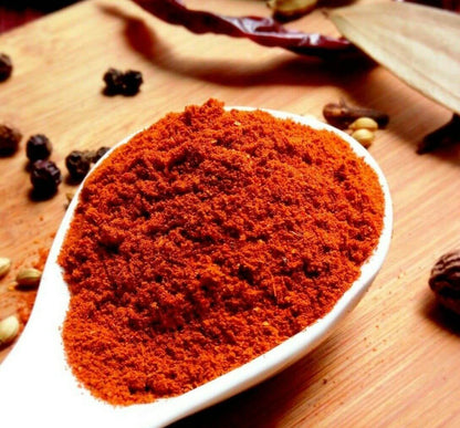 Natco Tandoori Masala in a white spoon, vibrant red spice blend for authentic tandoori cooking.