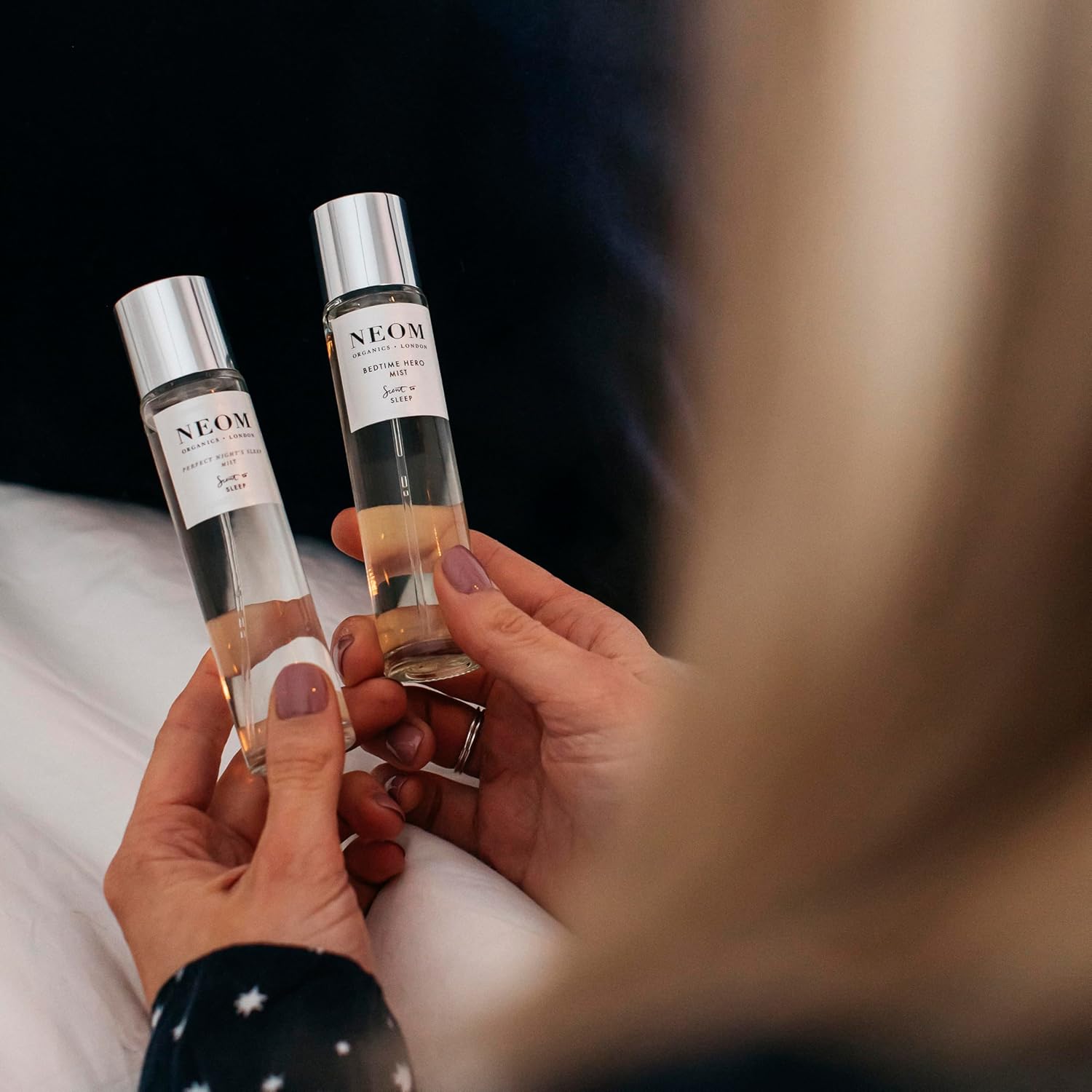 Two Neom skincare bottles held by a person with a blurred background