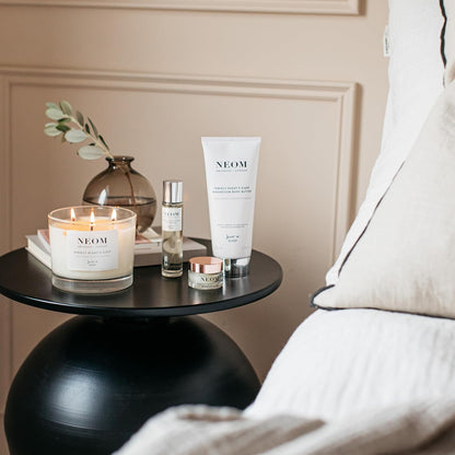 NEOM products including a candle, bottle, and tube on a table with a neutral background
