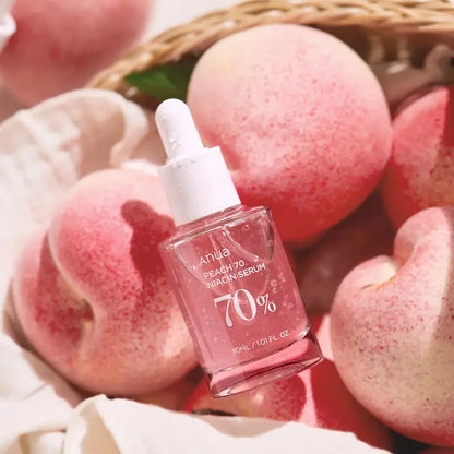 Anua Peach 70% Niacinamide Serum bottle surrounded by fresh peaches, promoting bright and hydrated skin.