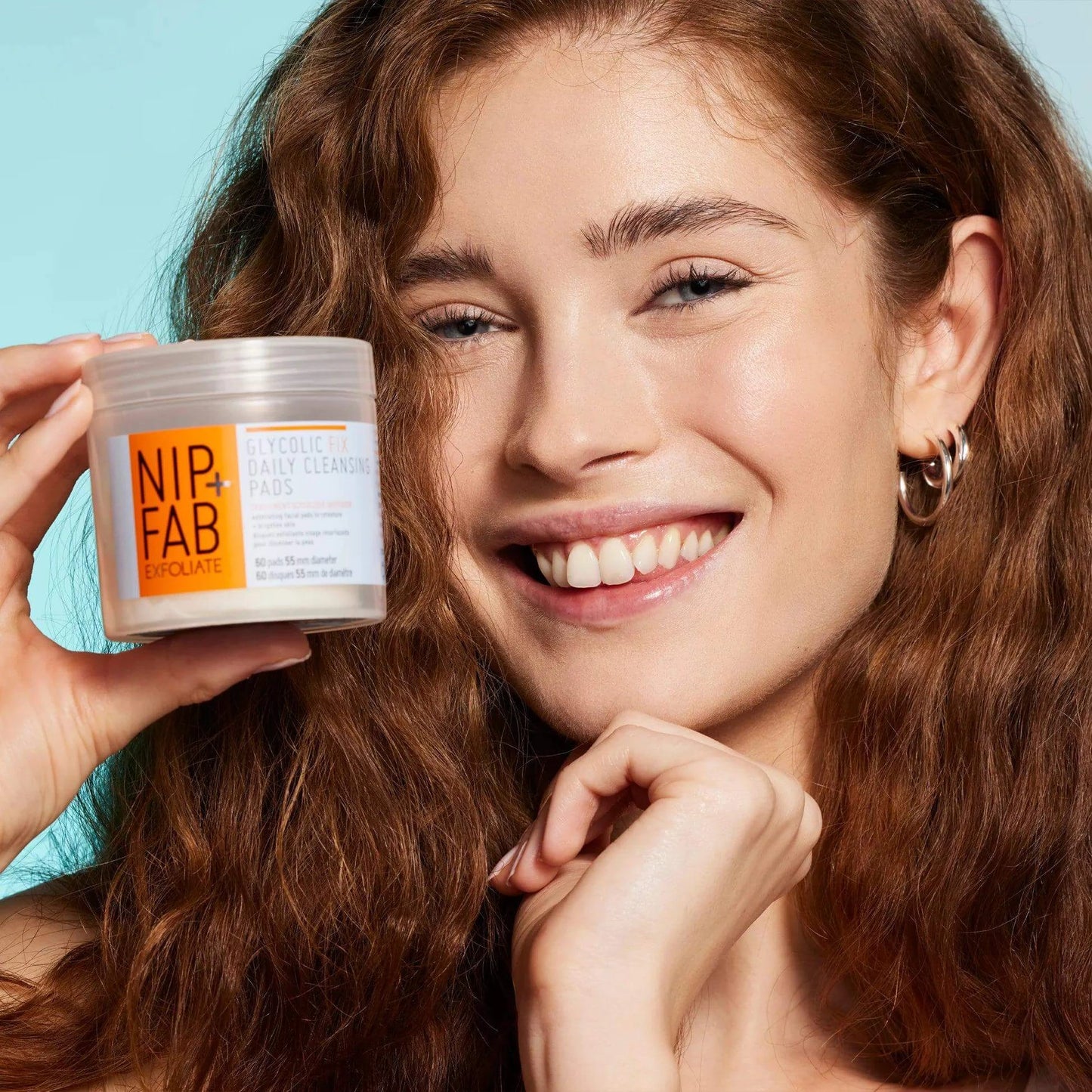 Nip + Fab Glycolic Fix Daily Cleansing Pads held by a smiling woman, showcasing anti-aging skincare.