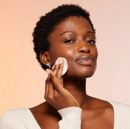 Woman applying Nip & Fab to her face with a cotton pad against a beige background