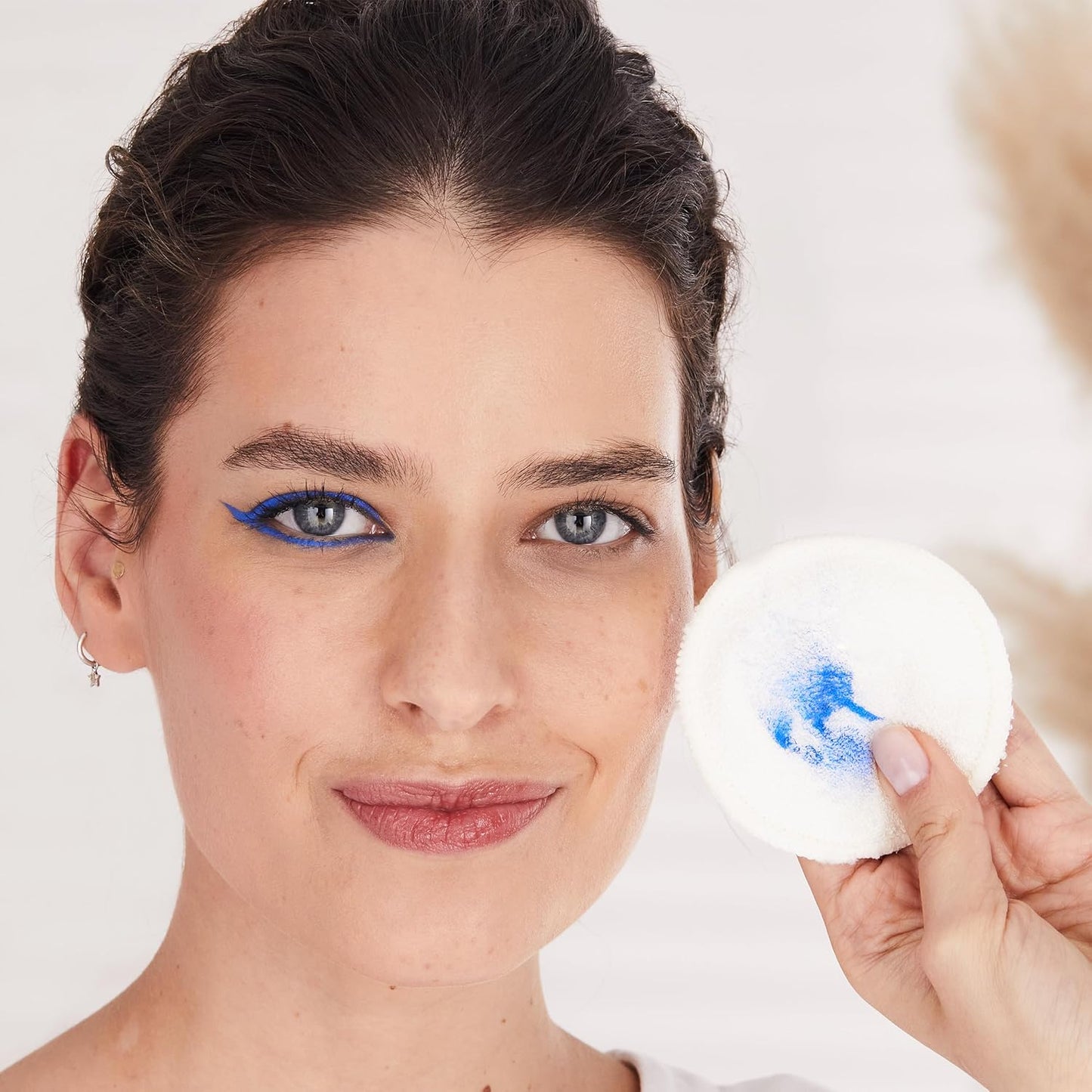 Woman holding a white NIVEA makeup puff with blue makeup residue against a plain background