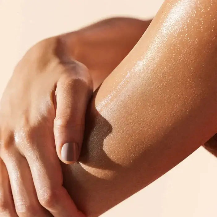 Close-up of a hand touching a smooth, sun-kissed arm against a beige background Nuxe