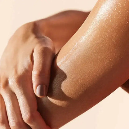 Close-up of a hand touching a smooth, sun-kissed arm against a beige background Nuxe
