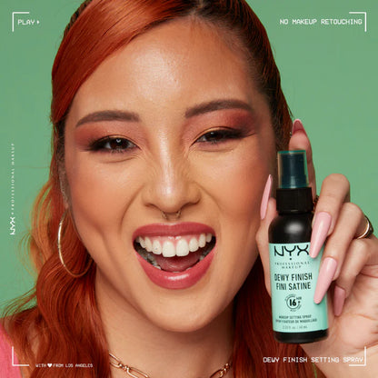 Woman holding a NYX Dewy Finish Setting Spray against a green background