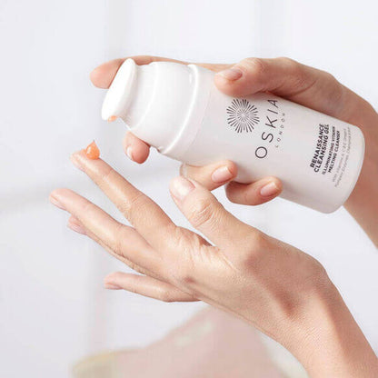 Hand holding a bottle of Oskia skincare product against a light background