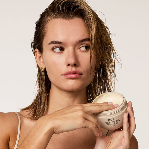 Woman holding OUAI hair product against a plain background