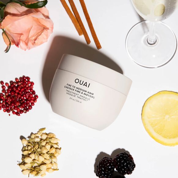 OUAI hair product jar on a white surface with flowers, candles, and fruit