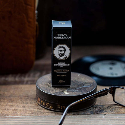 Percy Nobleman beard oil bottle on a wooden surface with glasses and a record player in the background