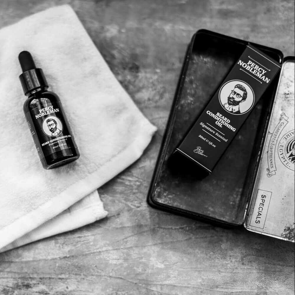 Black and white image of a Percy Nobleman beard oil bottle and grooming products on a textured surface.