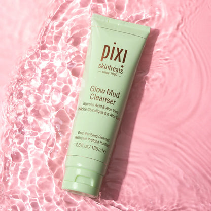 PIXI Glow Mud Cleanser 135ml tube on pink surface with water, enriched with Glycolic Acid and Aloe Vera for radiant skin.