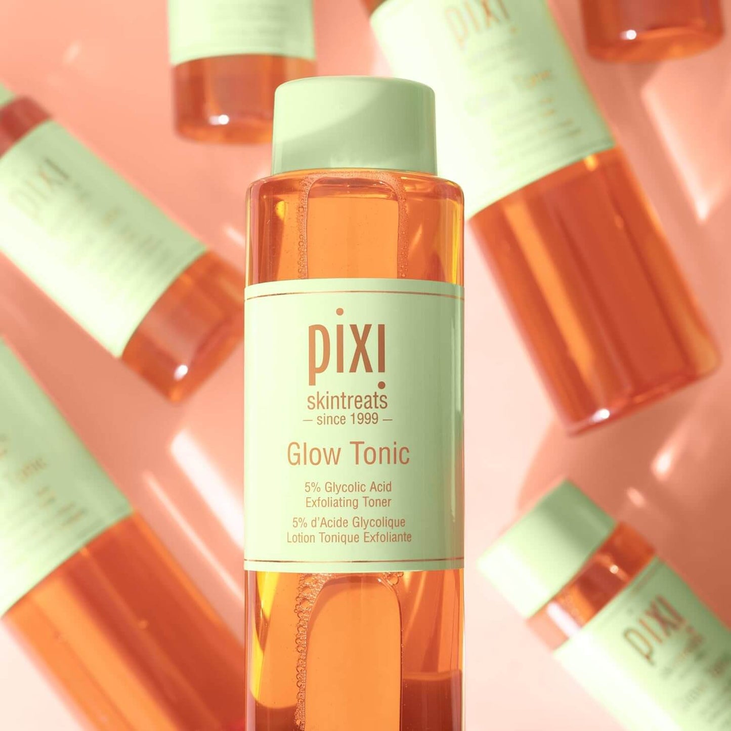 Bottle of PIXI Glow Tonic on a pink background with multiple bottles.