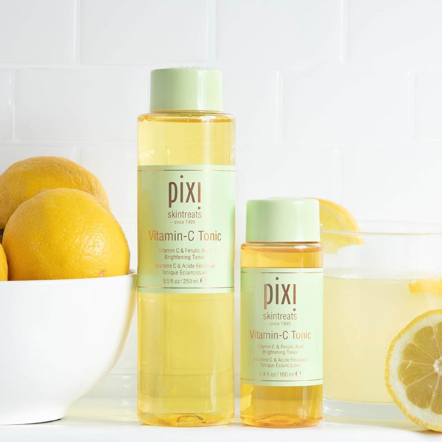 Two bottles of Pixi Vitamin-C Tonic with lemons on a white background
