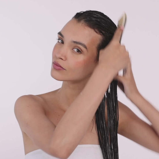 Woman applying Hair By Sam Mcknight Deeper Love Treatment Mask to wet hair, showcasing healthy hair care.