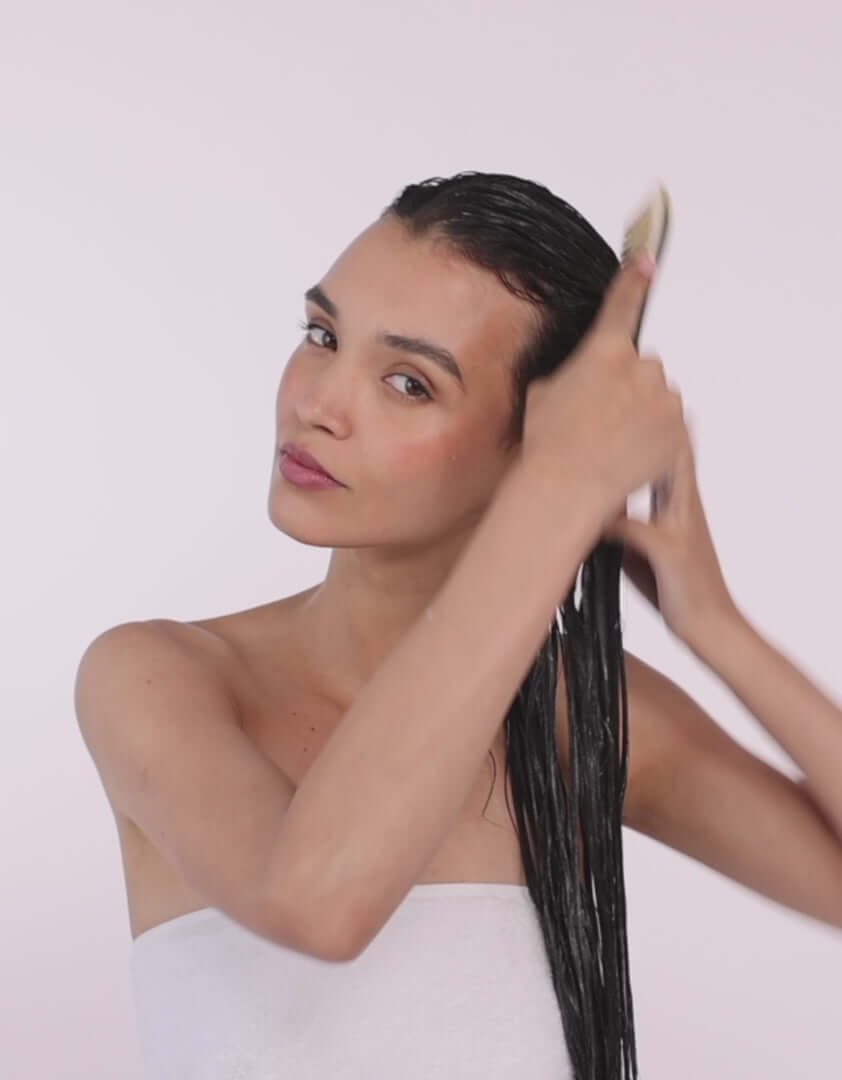 Woman applying Hair By Sam Mcknight Deeper Love Treatment Mask to wet hair, showcasing healthy hair care.