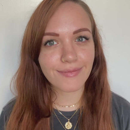 Woman with long red hair, wearing a sun graphic t-shirt and layered jewelry, smiling at the camera.