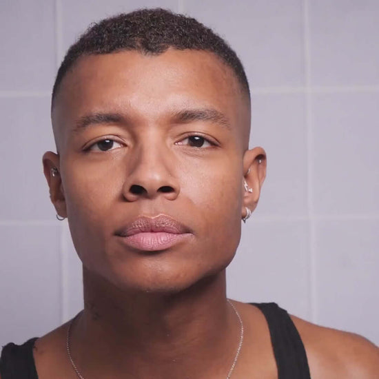 Close-up of a person with short hair and earrings, showcasing healthy skin and a neutral expression.