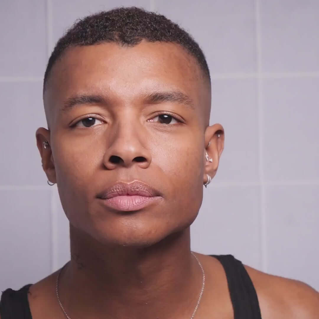 Close-up of a person with short hair and earrings, showcasing healthy skin and a neutral expression.