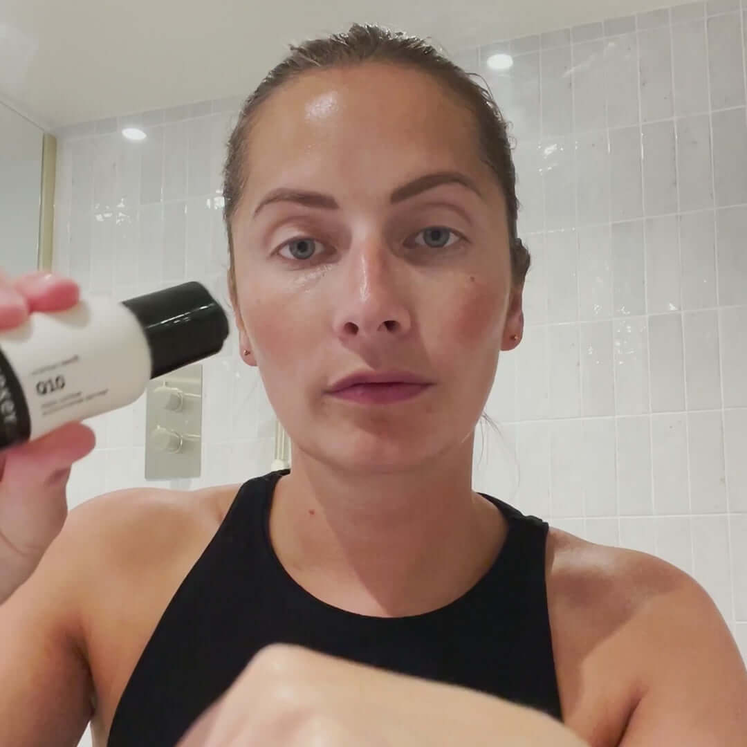 Woman applying The INKEY List Q10 Serum in a bathroom, showcasing radiant skin after skincare routine.