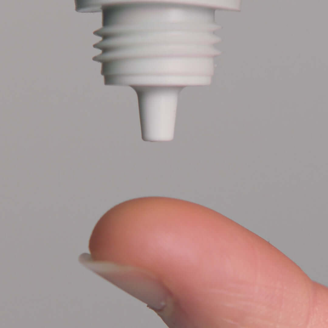 Close-up of a finger with a drop from a white skincare product nozzle, perfect for treating blemishes.