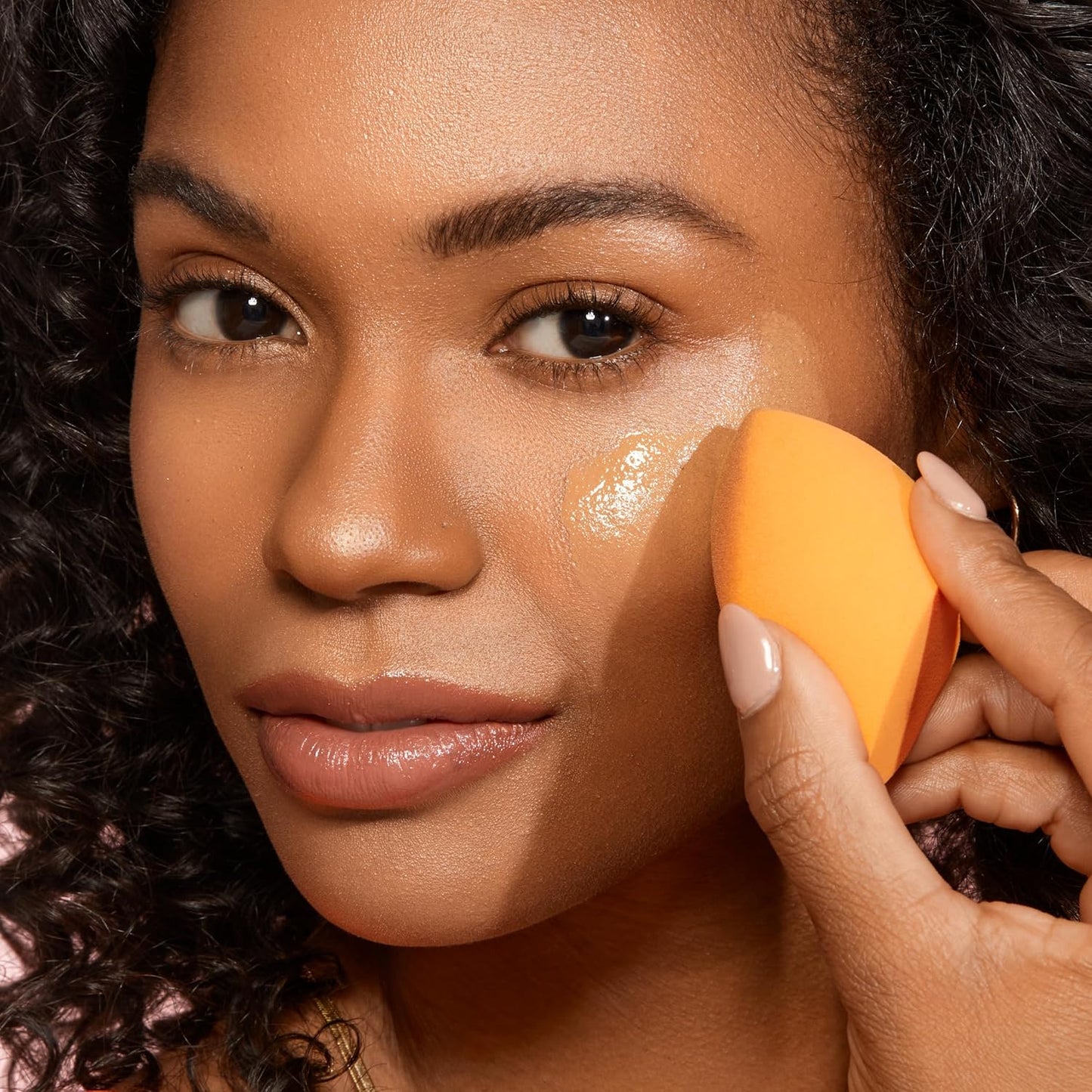 Woman applying makeup with an orange sponge on her face