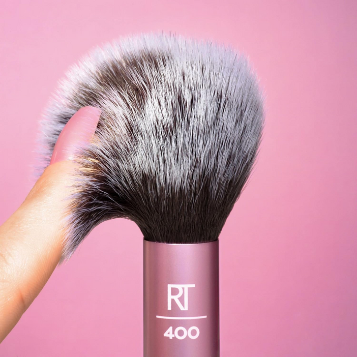 Real Techniques Blush Brush with soft, synthetic bristles being held against a pink background.