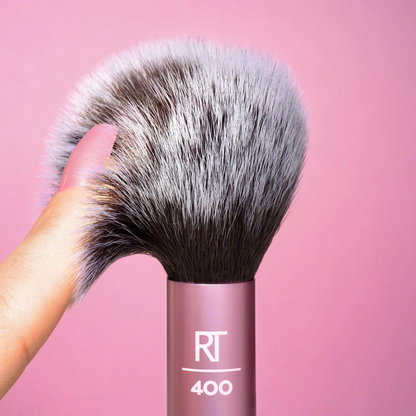 Real Techniques Blush Brush with soft, synthetic bristles being held against a pink background.