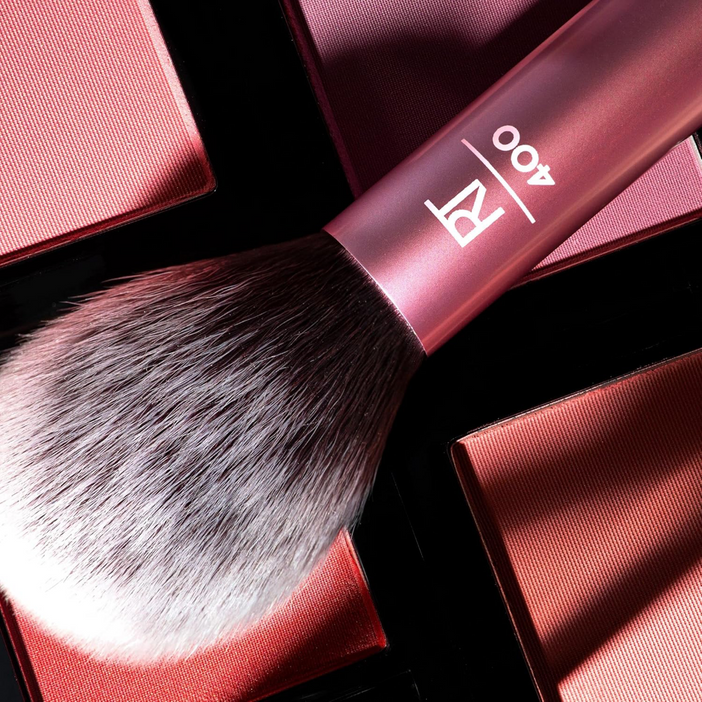 Real Techniques Blush Brush resting on blush palettes, showcasing its soft, hand-cut synthetic bristles for flawless application.
