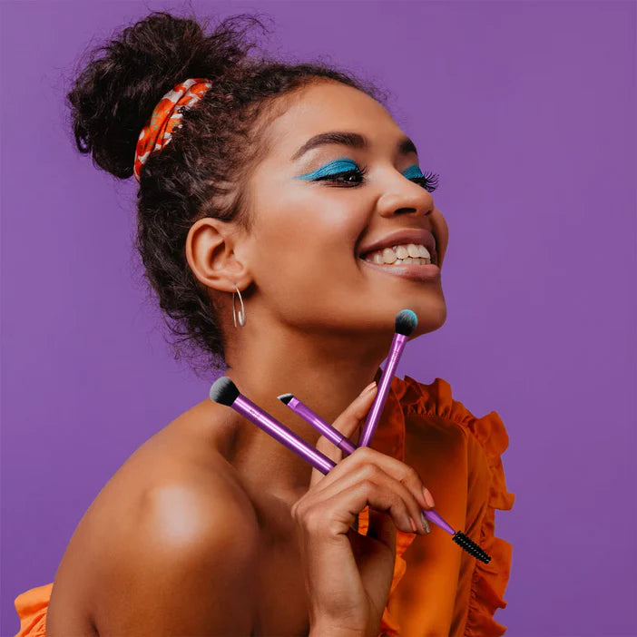 Woman holding makeup brushes against a purple background