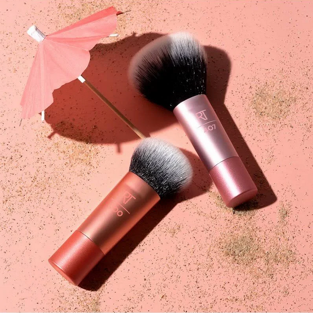 Two makeup brushes with pink and red handles on a pink textured background