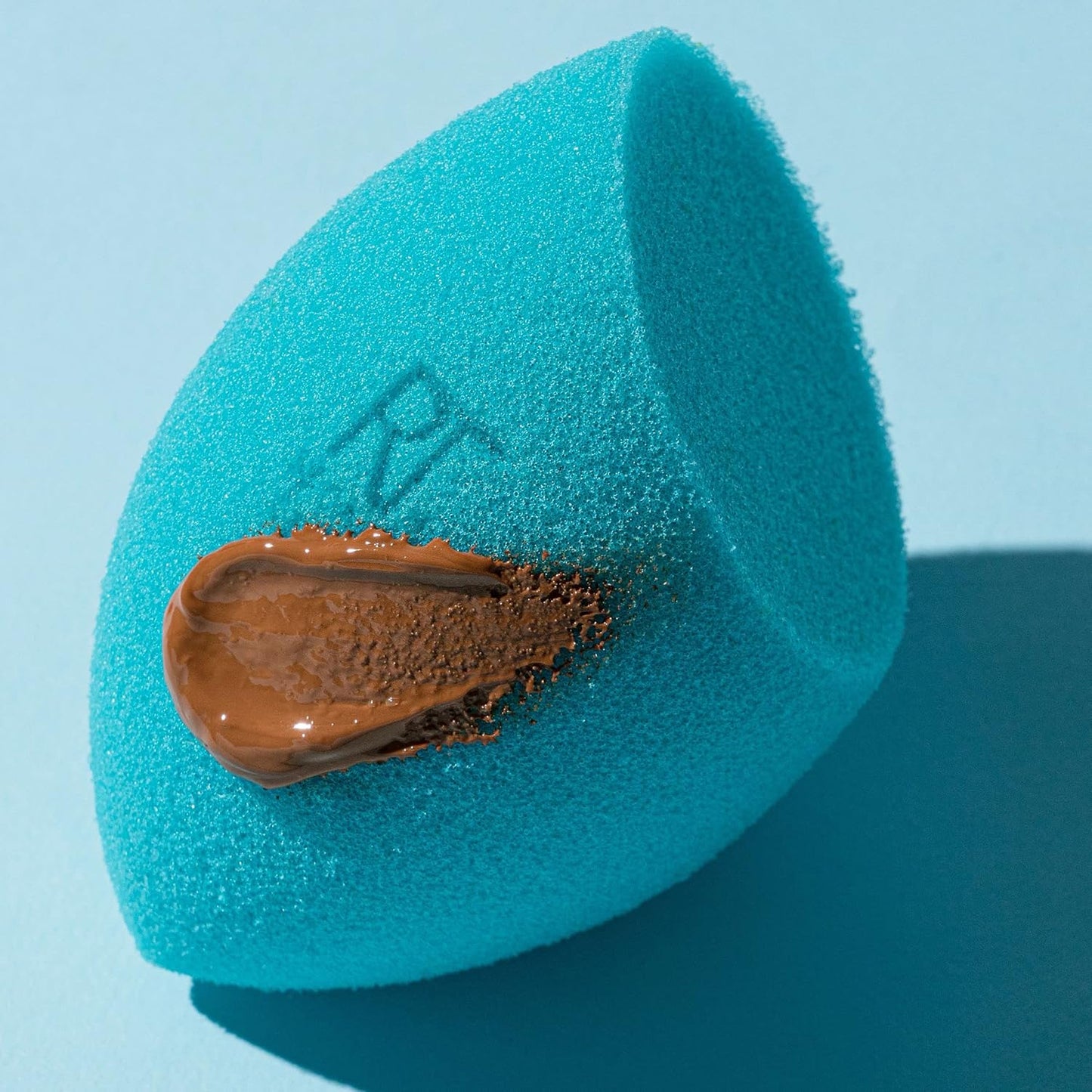 Blue makeup sponge with brown cosmetic product on a light blue background