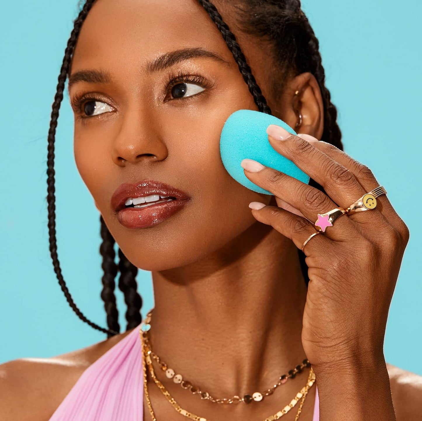 Woman applying a blue beauty blender to her face against a blue background