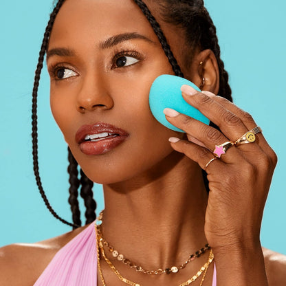Woman applying a blue beauty blender to her face against a blue background