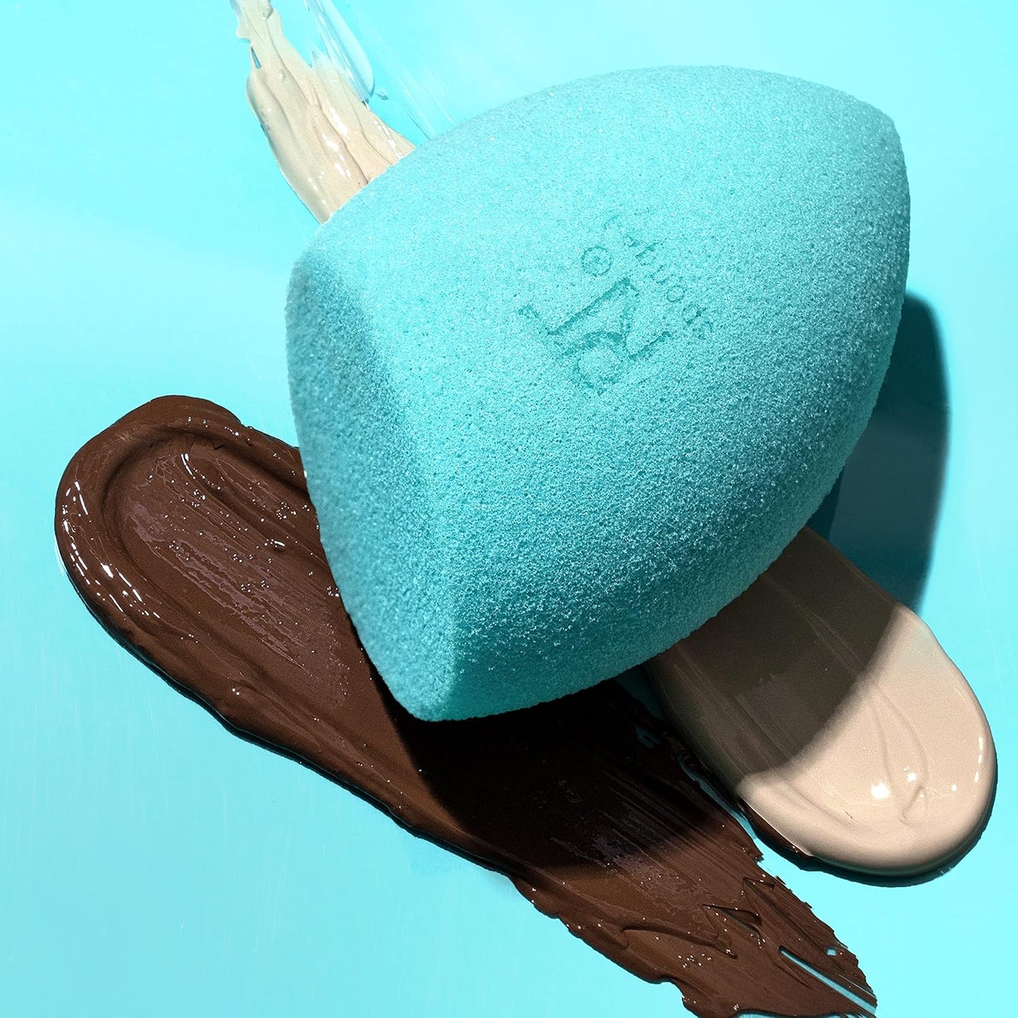 Turquoise makeup sponge with brand logo on a blue background with brown makeup smear