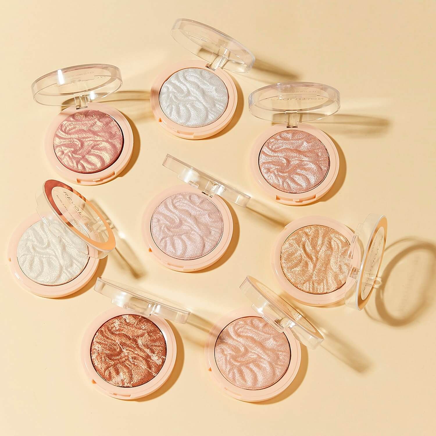 Multiple Revolution compact makeup powders with various shades on a beige background