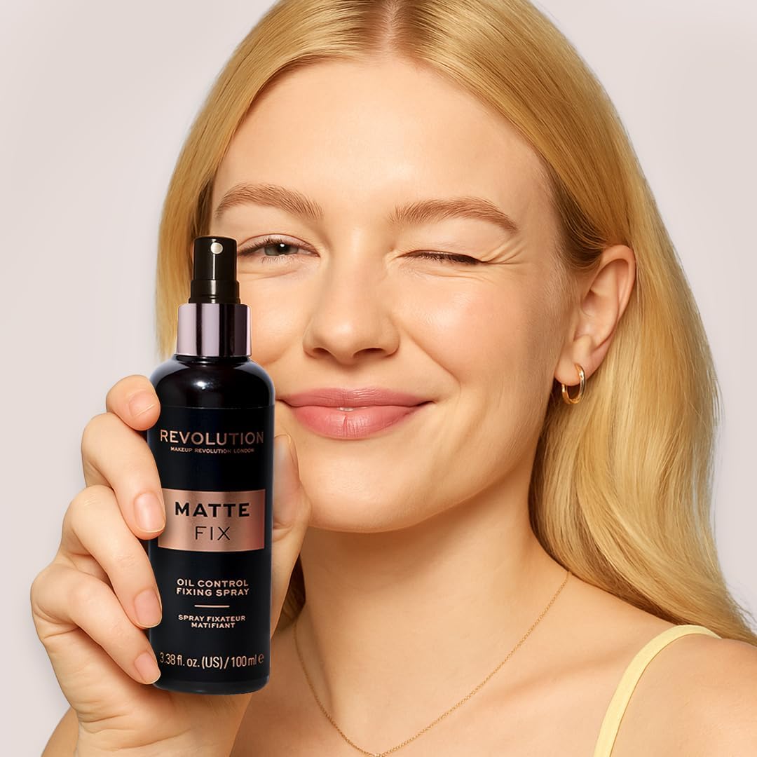Woman holding a Revolution Matte Fix oil control fixing spray against a plain background