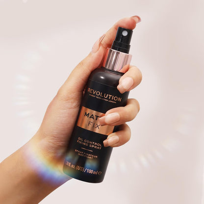 Hand holding a Revolution Mat Fix oil control fixing spray bottle against a light background