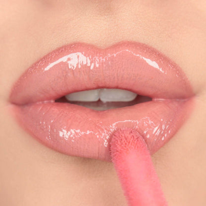 Makeup Revolution Close-up of lips with glossy, nude lip gloss being applied. Shade: Kiss from Revolution Pout Bomb collection.