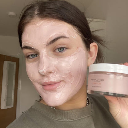 Woman with a pink face mask holding a Revolution product container.
