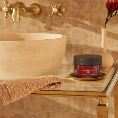 Bathroom setting with a jar of body cream, towel, and vase on a shelf.