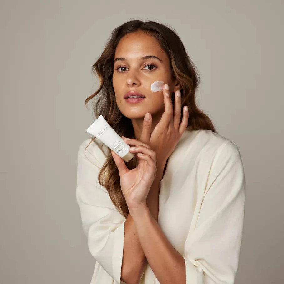 Model applying RITUALS The Ritual of Namaste Skin Brightening Face Exfoliator on her face for a radiant complexion.