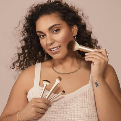 Woman holding makeup brushes against a neutral background