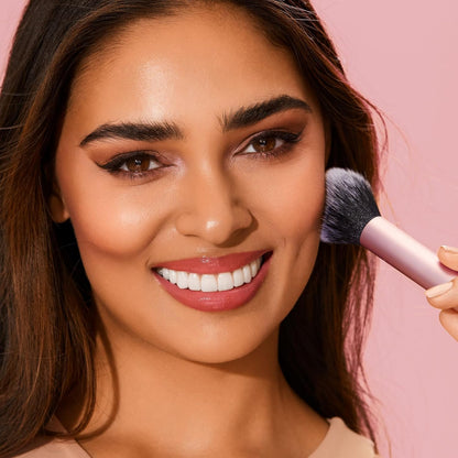 Woman applying makeup with a brush on a pink background