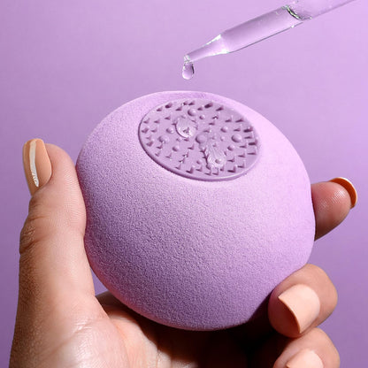 Purple textured ball held by a hand with a dropper of liquid above it on a purple background